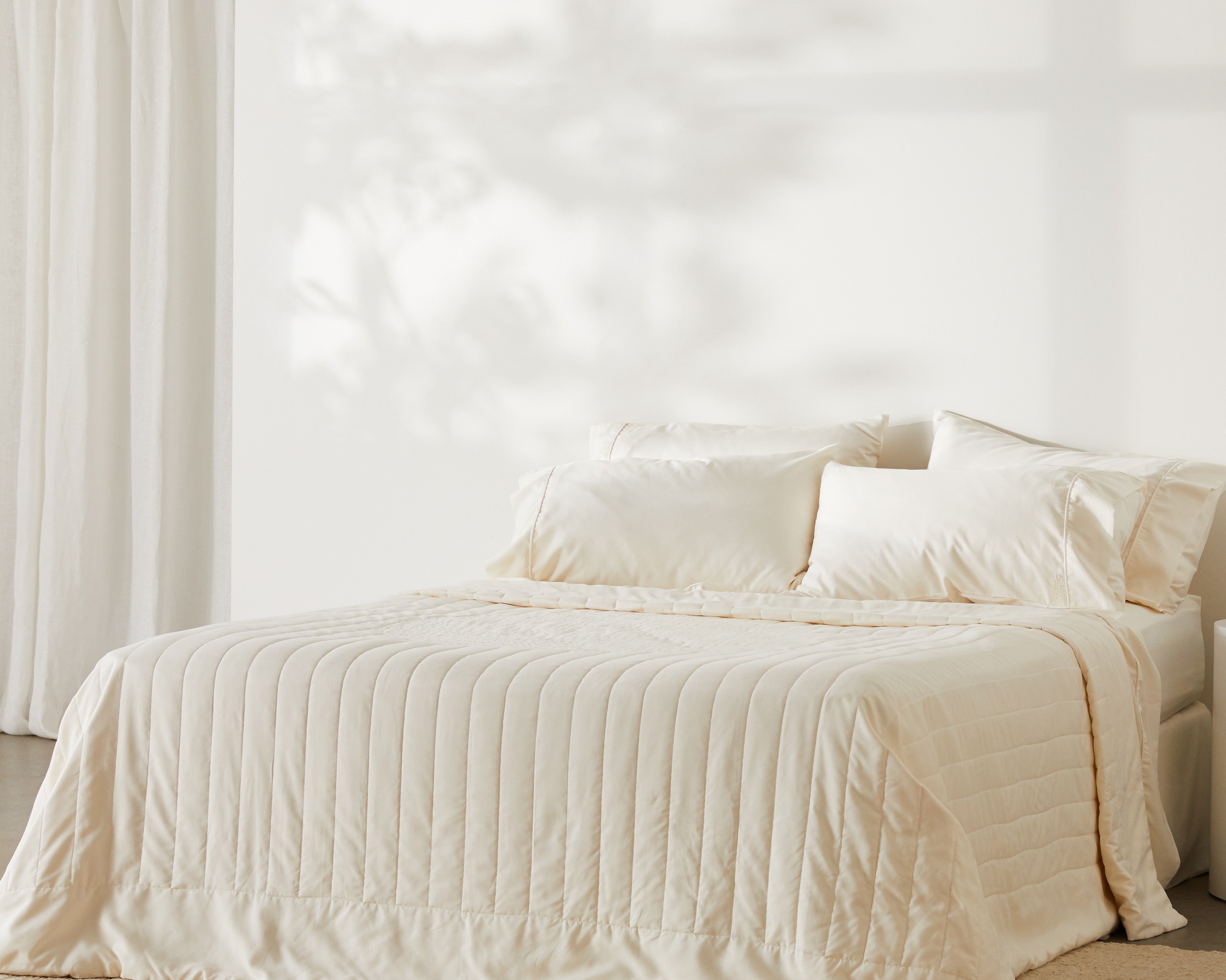 Bed made with ivory bamboo sheets, pillowcases and a quilted coverlet in a sunlit bedroom